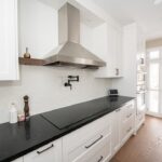 Modern white kitchen with black countertop and stainless steel chimney hood