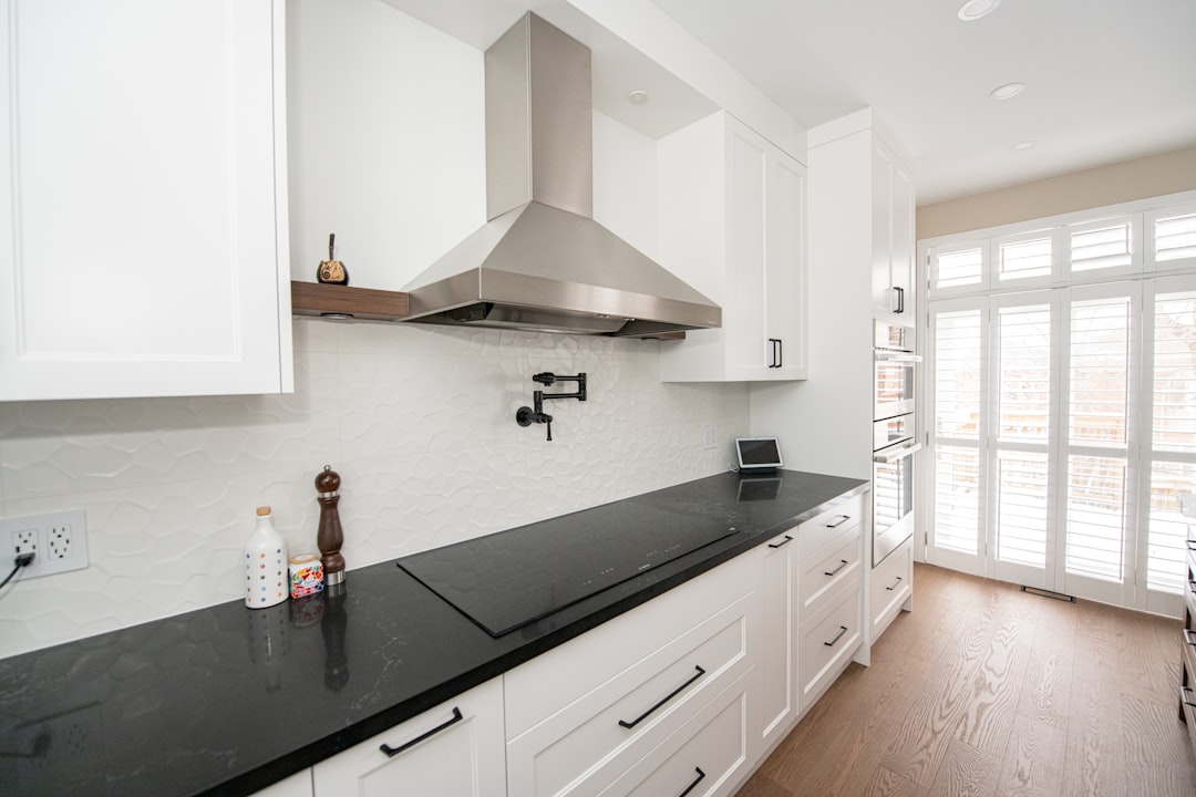 Modern white kitchen with black countertop and stainless steel chimney hood